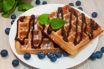 Belgian waffles on a plate with chocolate sauce and blueberries