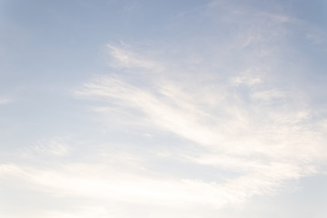 light blue sky with feather-like clouds lit by the rays of the early sun