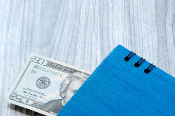 A twenty-dollar bill with a blue notebook. Wooden marble Board background. The problem of budgeting, calculation of estimates. The concept of profitable investment.