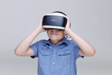 Young happy boy in glasses of virtual reality on gray background. Augmented reality, game, future technology concept. VR.