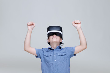 Young happy boy in glasses of virtual reality on gray background. Augmented reality, game, future technology concept. VR.