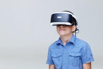 Young happy boy in glasses of virtual reality on gray background. Augmented reality, game, future technology concept. VR.