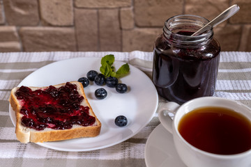 The toast with blueberry jam and a can with huckleberry jam on a light background