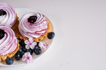 Sweet tartlet with meringue and blueberry and huckleberry jam and phlox flowers on white background closeup
