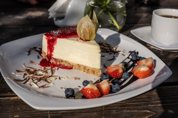 classic cheesecake with raspberry jam on a plate decorated with fresh strawberries and cup of coffee