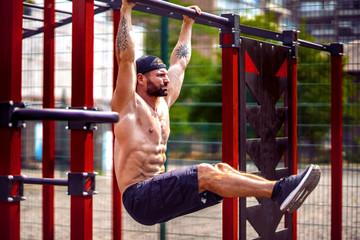 Strong Muscular bearded man doing abdominal exercise on horizontal bar at street gym yard. Strength...