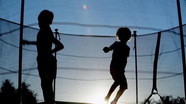 Silhouette of Kids jumping inside trampoline during sunset sunlight flare