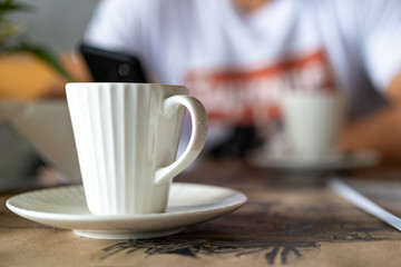 one ceramic cup of coffee in the foreground on a blurred background of the second cup and a man with a phone in his hand