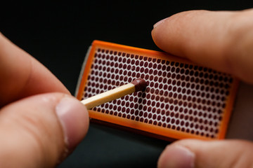 Man's fingers lighting a match, setting fire on friction. On a black background. Matches and fire....