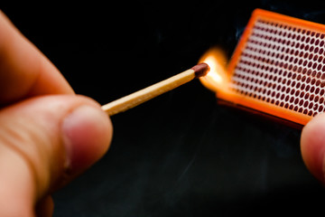 Man's fingers lighting a match, setting fire on friction. On a black background. Matches and fire....