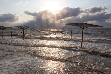 Fototapeta na wymiar Sea waves flood the beach with umbrellas during a storm on the sea on a summer evening. Sea of Azov, Krasnodar Territory, Russia.