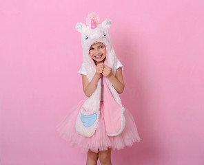 Caucasian beautiful little girl in a hat with  unikorn  on a pink background.