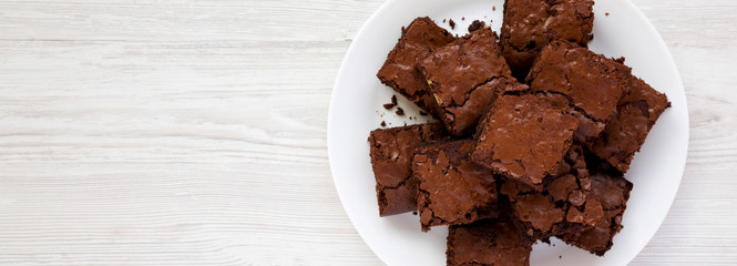 Homemade chocolate brownies on a white plate on a white wooden background, top view. Flat lay, overhead, from above. Space for text.