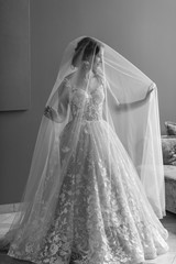 Black and white portrait of beautiful bride in wedding dress touchs and throws her veil up in hotel.