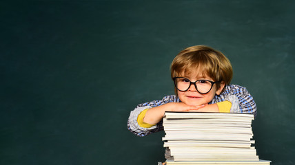 Funny little boy pointing up on blackboard. School concept. School kids against green chalkboard. Learning concept. Happy mood smiling broadly in school