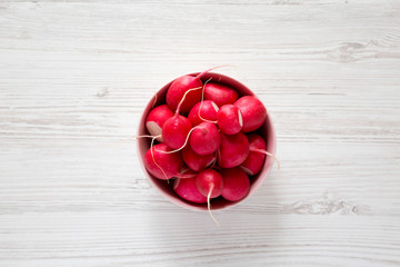 Fresh radishes in a pink bowl on a white wooden background, top view. Flat lay, overhead, from above.