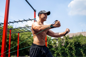 Fitness man training chest with resistance bands at street gym yard. Strength and motivation....