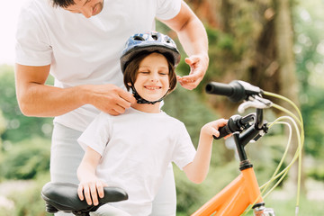 Naklejka premium cropped view of father putting helmet on son while boy smiling and standing near bicycle