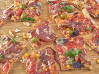 Pizza on thin dough.With slices of salami and ham ,olives and tomatoes.On a background of vegetables.
