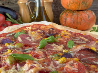 Pizza on thin dough.With slices of salami and ham ,olives and tomatoes.On a background of vegetables.