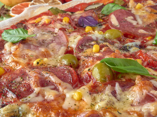 Pizza on thin dough.With slices of salami and ham ,olives and tomatoes.On a background of vegetables.