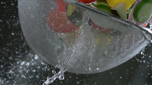 Pieces of fresh delicious food vegetable mixture is washed in a colander with a jet of water. Vegetarian menu concept. Slow motion