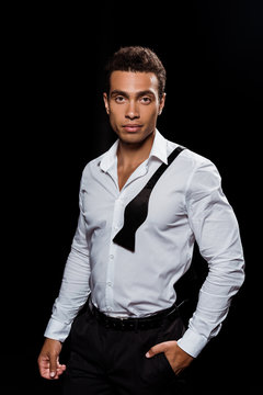 handsome mixed race man looking at camera while standing with hand in pocket isolated on black