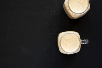 Peanut butter banana smoothie in glass jars on a black background, top view. Overhead, flat lay, from above. Copy space.