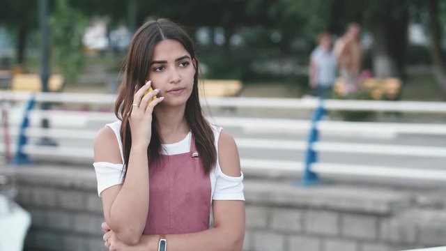 Beautiful girl frowning, fuming and talking on phone on Dnipro quay in slo-mo 