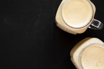 Peanut butter banana smoothie in glass jars on a black background, overhead view. Overhead, flat lay, from above. Copy space.