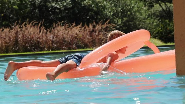 Small boy at the swimming pool on top of inflatable mattress playing