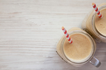 Peanut butter banana smoothie in glass jars on a white wooden background, overhead view. Top view, flat lay, from above. Copy space.