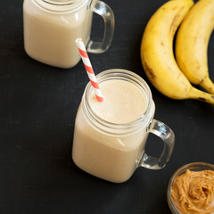 Mason glass jar mugs filled with peanut butter banana smoothie on a black background, low angle...