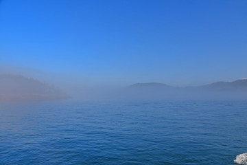 Naklejka na ściany i meble Morning fog hugs the coast of Deception Pass as it enters the Salish Sea in Washington State