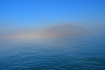 Morning fog hugs the coast of Deception Pass as it enters the Salish Sea in Washington State