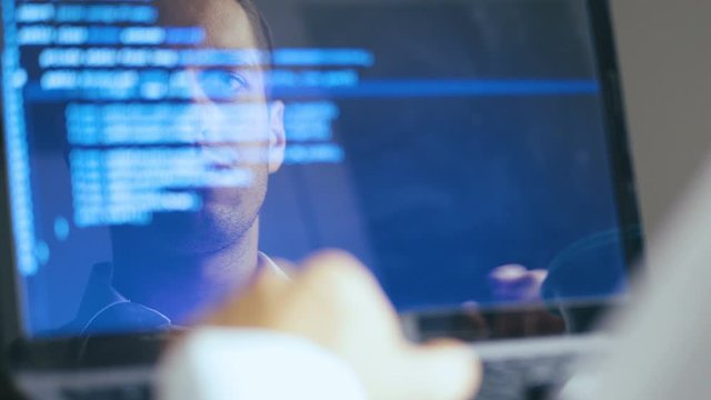 Double Exposure Shot of Man Hacker Programmer working at a laptop. Reflection in monitor: Developer writes blue code.