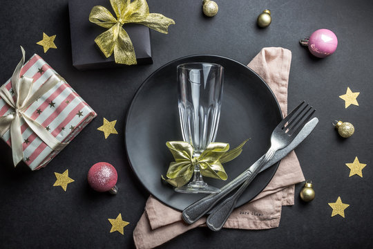 Christmas table setting with plate, silverware and decorations over black background