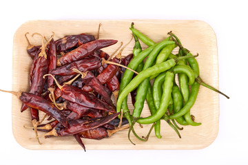 Tray with dried red chillies and fresh green chillies on a white background