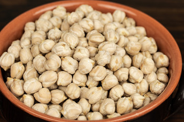 Raw chickpeas in a ceramic bowl on a dark  wooden  background. top center view, out of range.