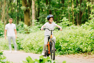 Naklejka premium selective focus of happy boy riding bicycle and father standing and looking at son