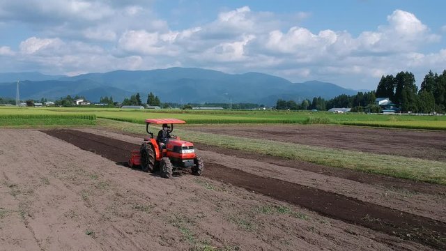 トラクターで農地を耕す日本人の男性　農業