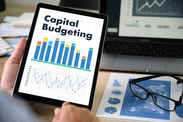 capital budgeting Business team hands at work with financial reports and a laptop, top view