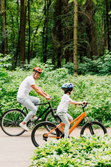 Fototapeta premium full length view of father and son riding bicycles while dad looking at boy bicycle wheel