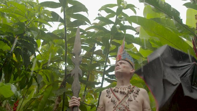 Caucasian Adult Man Dressed Up As Indigenous Using Umbrella To Protect Himself From Rain In Jungle In Ecuador