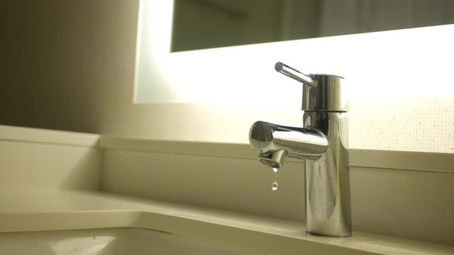 Leaky faucet in modern bathroom with illuminating mirror