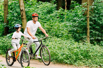 Naklejka premium father and son smiling while riding bicycles around forest