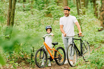 Naklejka premium full length view of father and son standing in forest with bicycles while man screaming