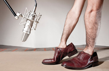Step Foley on wood.  Man hands inside male dress shoes front a professional microphone and over a wood table.