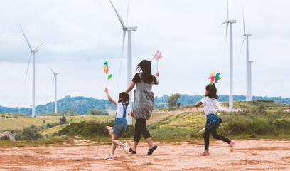 Two asian child girls and their mother are running and playing with wind turbine toy together with fun in the wind turbine field