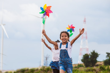 Two asian child girls are running and playing with wind turbine toy together with fun at wind...